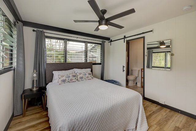 bedroom with light hardwood / wood-style flooring, ceiling fan, ensuite bathroom, and a barn door