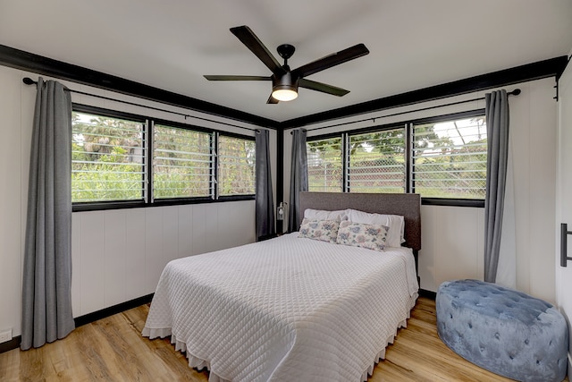 bedroom featuring ceiling fan, wooden walls, light hardwood / wood-style flooring, and multiple windows