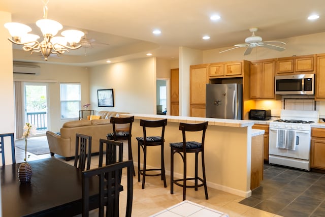 kitchen with tile patterned floors, ceiling fan with notable chandelier, stainless steel appliances, pendant lighting, and tile counters