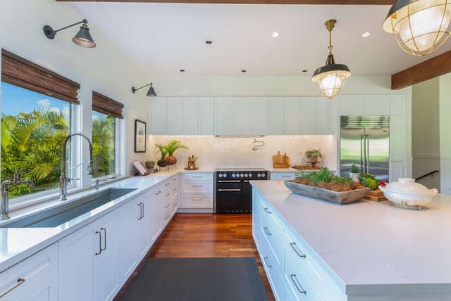 kitchen with stainless steel built in refrigerator, sink, decorative light fixtures, dark wood-type flooring, and white cabinetry