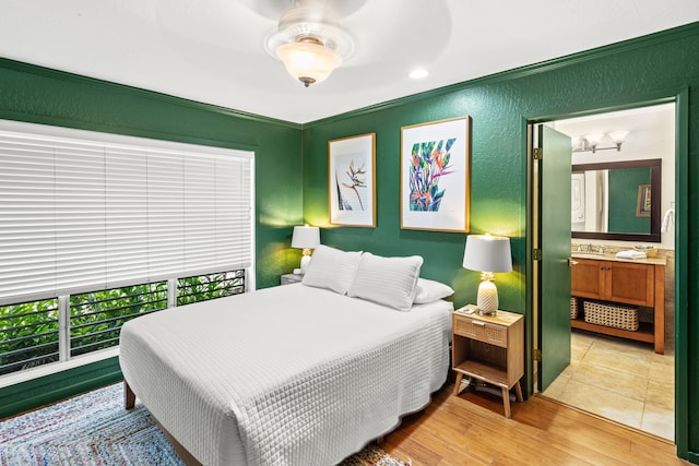 bedroom featuring ceiling fan, connected bathroom, sink, ornamental molding, and light hardwood / wood-style flooring