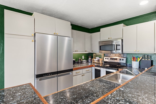 kitchen featuring a textured ceiling, stainless steel appliances, decorative backsplash, and white cabinetry