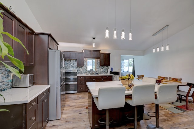 kitchen featuring light hardwood / wood-style floors, vaulted ceiling, backsplash, white fridge, and decorative light fixtures