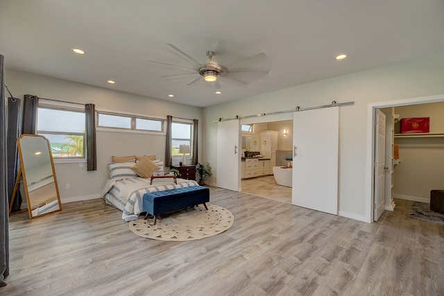 bedroom featuring connected bathroom, light hardwood / wood-style flooring, a spacious closet, a barn door, and ceiling fan