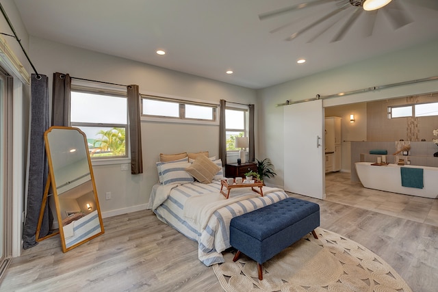 bedroom with a barn door, light hardwood / wood-style flooring, and ceiling fan