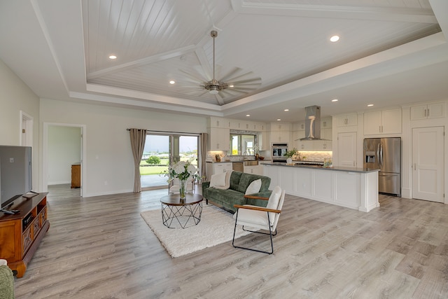 living room with lofted ceiling with beams, a tray ceiling, light wood-type flooring, and ceiling fan