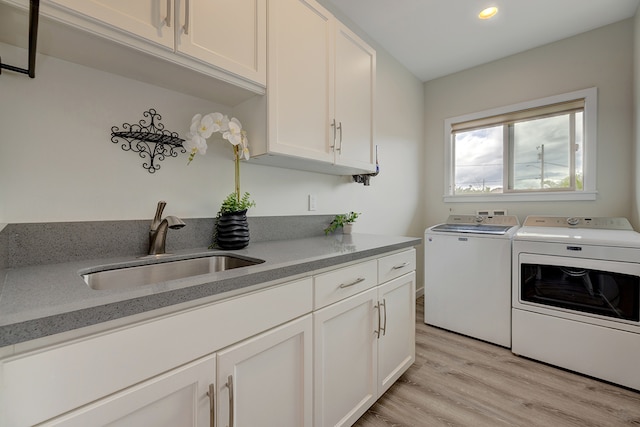 washroom featuring sink, cabinets, light hardwood / wood-style flooring, and washing machine and clothes dryer