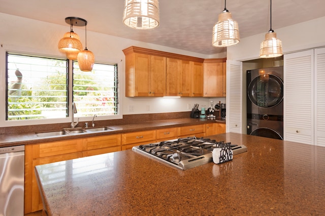 kitchen featuring stainless steel appliances, stacked washer / drying machine, hanging light fixtures, and sink