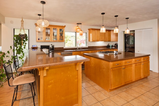 kitchen with appliances with stainless steel finishes, a kitchen breakfast bar, stacked washing maching and dryer, kitchen peninsula, and pendant lighting