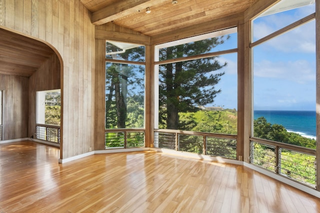 unfurnished sunroom with vaulted ceiling with beams, plenty of natural light, a water view, and wooden ceiling