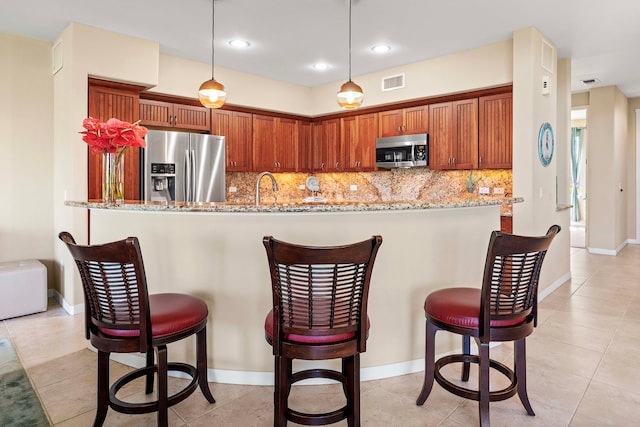 kitchen featuring light stone counters, stainless steel appliances, hanging light fixtures, and kitchen peninsula