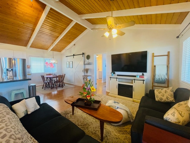 living room with ceiling fan, light wood-type flooring, a barn door, and beam ceiling