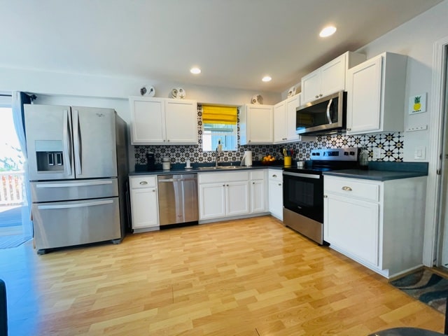 kitchen with white cabinets, sink, tasteful backsplash, light hardwood / wood-style flooring, and appliances with stainless steel finishes