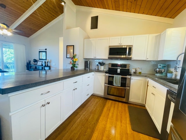 kitchen with tasteful backsplash, white cabinets, kitchen peninsula, appliances with stainless steel finishes, and wooden ceiling