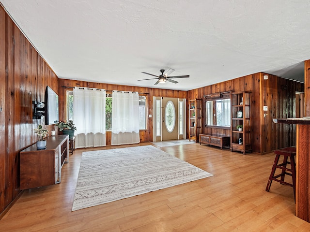 living room featuring ceiling fan, wooden walls, and light wood-type flooring