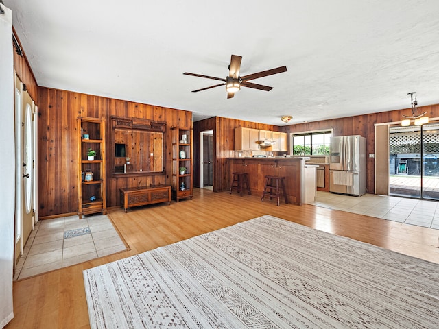 unfurnished living room featuring light hardwood / wood-style floors, wood walls, and ceiling fan