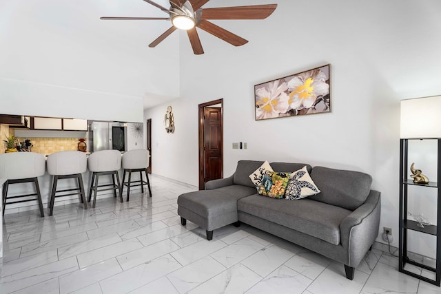 living area with ceiling fan, a towering ceiling, baseboards, and marble finish floor