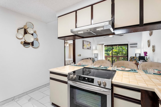 kitchen featuring a wall unit AC, stainless steel electric range, white cabinets, exhaust hood, and a textured ceiling