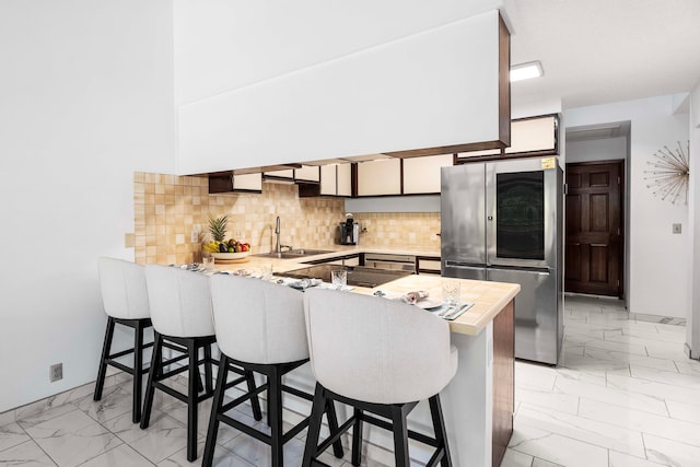 kitchen with a peninsula, a sink, high end refrigerator, light countertops, and marble finish floor
