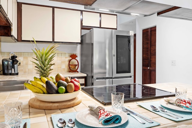 kitchen featuring white cabinets, tile countertops, decorative backsplash, and stainless steel fridge