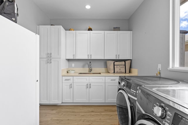 laundry area with washer and clothes dryer, cabinets, light hardwood / wood-style floors, and sink