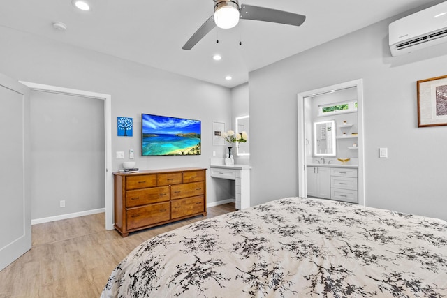 bedroom with ceiling fan, connected bathroom, sink, light hardwood / wood-style flooring, and a wall unit AC