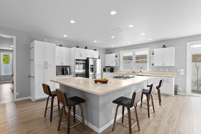 kitchen featuring light wood-type flooring, stainless steel appliances, white cabinets, a kitchen bar, and a spacious island