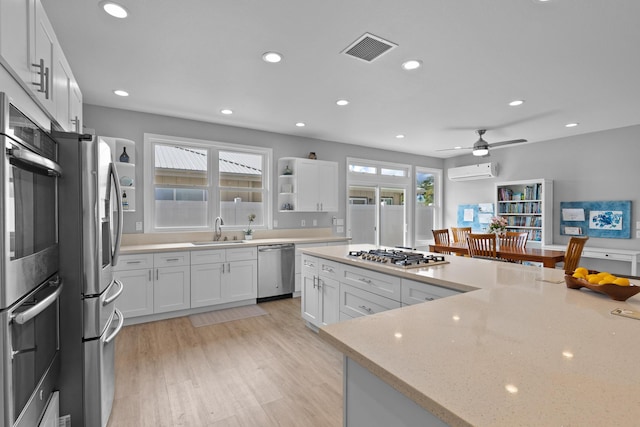 kitchen with light stone counters, stainless steel appliances, white cabinets, light hardwood / wood-style flooring, and a wall mounted AC