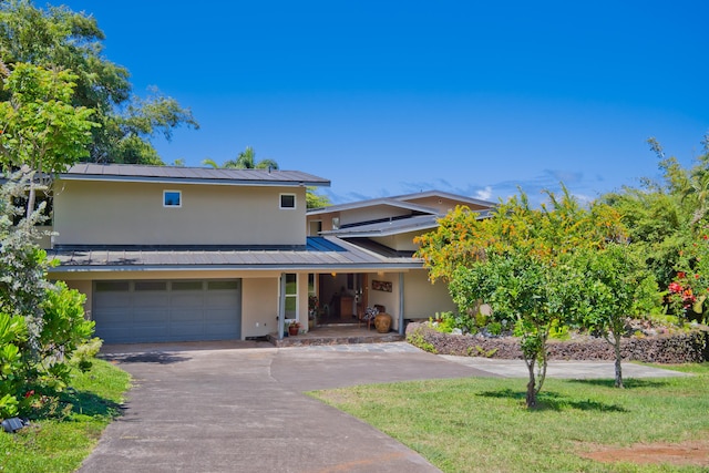 traditional-style house featuring a front yard, metal roof, a garage, stucco siding, and driveway