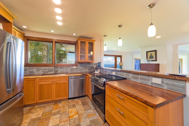 kitchen with kitchen peninsula, sink, tasteful backsplash, decorative light fixtures, and stainless steel appliances