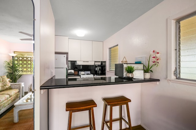 kitchen featuring ceiling fan, white refrigerator, kitchen peninsula, white cabinetry, and a kitchen bar