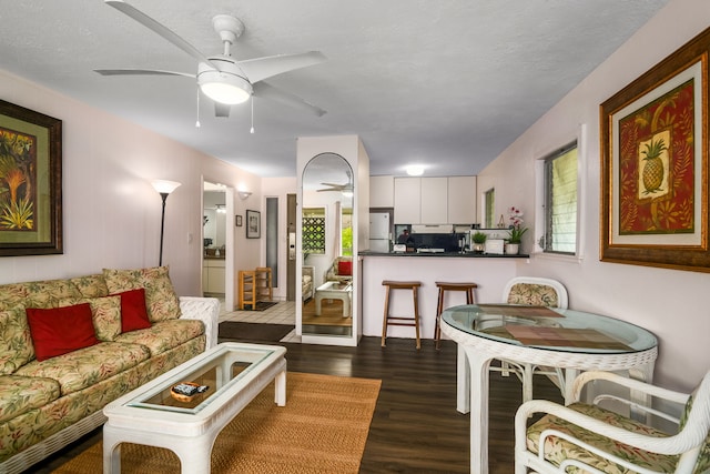 living room featuring ceiling fan, a textured ceiling, and dark hardwood / wood-style floors