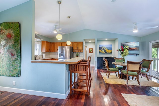 kitchen featuring kitchen peninsula, stainless steel fridge, vaulted ceiling, dark hardwood / wood-style floors, and hanging light fixtures