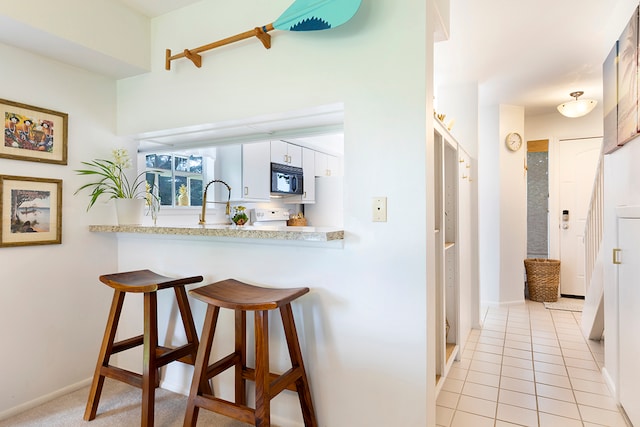 kitchen with kitchen peninsula, white range oven, white cabinetry, a breakfast bar area, and light tile patterned floors