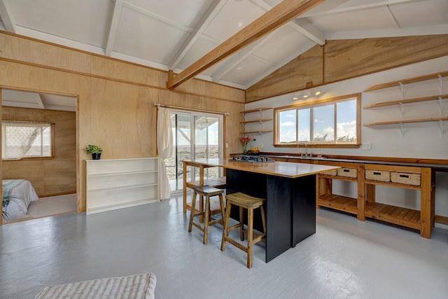 kitchen featuring wood walls, beam ceiling, a kitchen bar, and a wealth of natural light