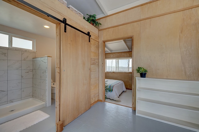 bathroom with tiled shower, wooden walls, and toilet