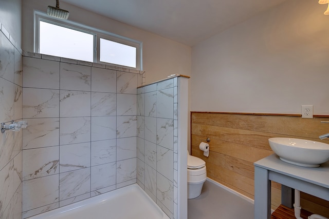 bathroom with wood walls, sink, tiled shower, and toilet