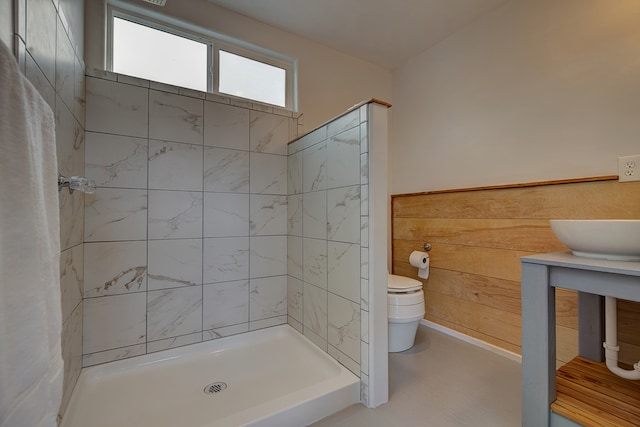 bathroom with wooden walls, a tile shower, toilet, and vanity