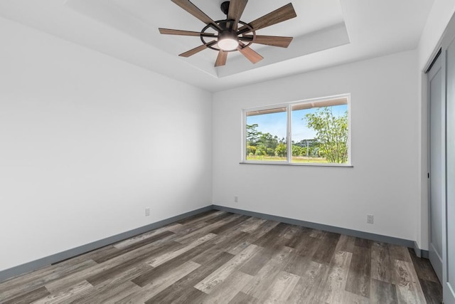 unfurnished bedroom with a raised ceiling, baseboards, a closet, and wood finished floors