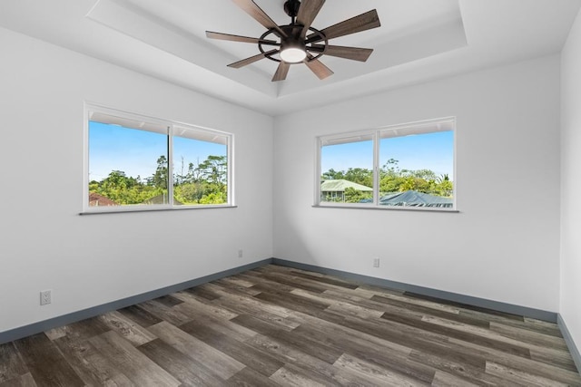 spare room with baseboards, a tray ceiling, dark wood finished floors, and ceiling fan