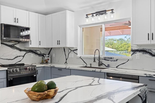 kitchen with light stone countertops, stove, sink, and white cabinets