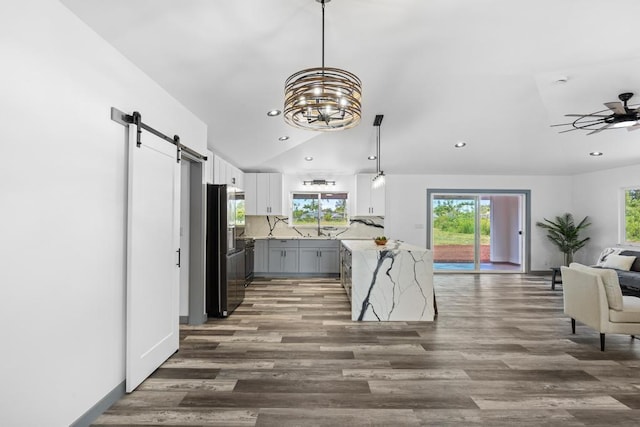 interior space with pendant lighting, dark hardwood / wood-style floors, ceiling fan with notable chandelier, white cabinetry, and a barn door