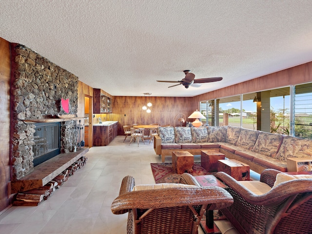 tiled living room featuring wood walls, ceiling fan, a fireplace, and a textured ceiling