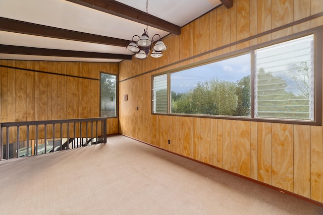 carpeted empty room with beamed ceiling, a notable chandelier, and wood walls