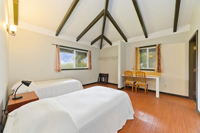 bedroom featuring vaulted ceiling with beams, wood-type flooring, and multiple windows