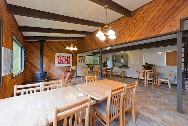 dining area with vaulted ceiling with beams, a notable chandelier, a wood stove, and wooden walls