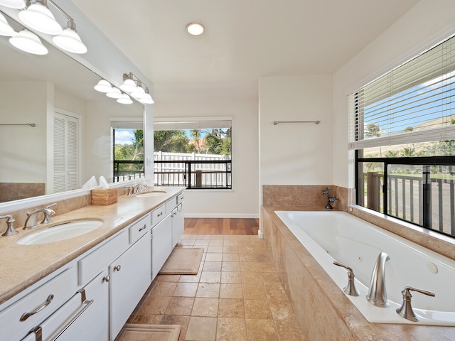 bathroom featuring tiled tub, vanity, and a notable chandelier