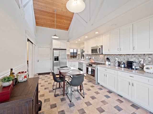 kitchen with hanging light fixtures, backsplash, white cabinetry, appliances with stainless steel finishes, and light stone countertops