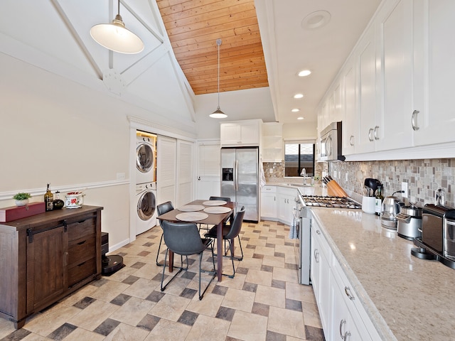 kitchen featuring decorative light fixtures, stacked washing maching and dryer, white cabinetry, appliances with stainless steel finishes, and vaulted ceiling