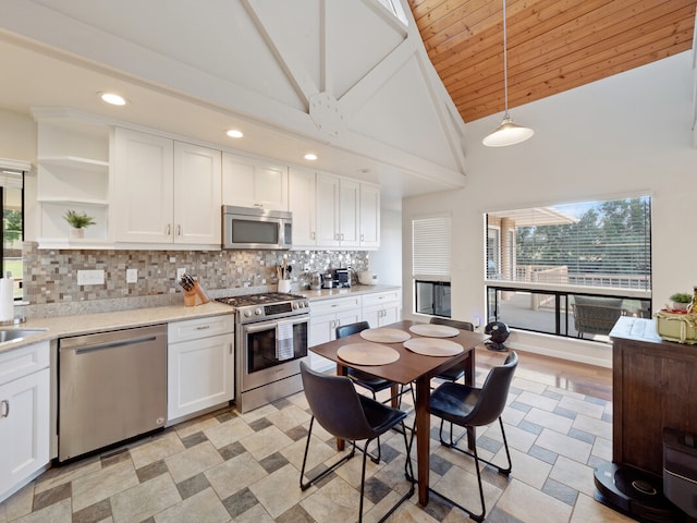 kitchen featuring tasteful backsplash, white cabinets, high vaulted ceiling, appliances with stainless steel finishes, and decorative light fixtures